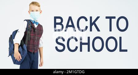 Bildungskonzept. Ein Schuljunge mit einer medizinischen Maske auf seinem Gesicht hält einen Schulrucksack, daneben steht der Text - ZURÜCK ZUR SCHULE Stockfoto