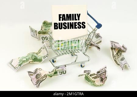 Business- und Economy-Konzept. Zerknitterte Dollars liegen auf einer weißen Oberfläche, da ist ein Wagen in einem Schild mit der Inschrift - FAMILIENUNTERNEHMEN Stockfoto