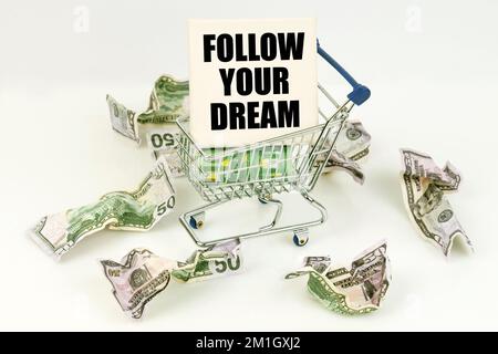 Business- und Economy-Konzept. Zerknitterte Dollars liegen auf einer weißen Oberfläche, da ist ein Wagen in einem Schild mit der Inschrift - FOLGE DEINEM TRAUM Stockfoto