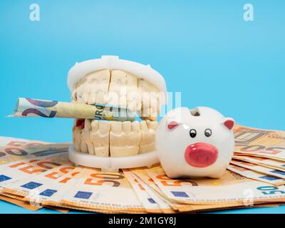 Zahngips, Sparschwein und Banknoten auf blauem Hintergrund. Gipsmodell der Zähne. Nahaufnahme. Stockfoto