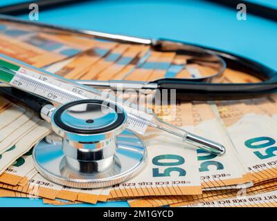 Medizinisches Stethoskop, Thermometer und Banknoten auf blauem Hintergrund. Nahaufnahme. Stockfoto