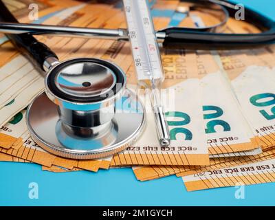 Medizinisches Stethoskop, Thermometer und Banknoten auf blauem Hintergrund. Nahaufnahme. Stockfoto