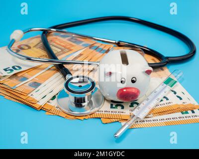 Medizinisches Stethoskop, Sparschwein, Thermometer und Banknoten auf blauem Hintergrund. Nahaufnahme. Stockfoto