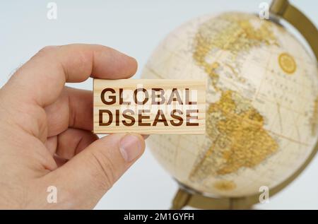 Globalisierungskonzept. Ein Mann hält in seiner Hand eine Holzplatte, auf der es steht - GLOBALE KRANKHEIT. Im Hintergrund ist ein Globus. Stockfoto