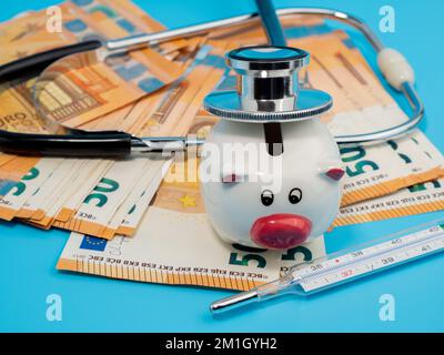 Medizinisches Stethoskop, Sparschwein, Thermometer und Banknoten auf blauem Hintergrund. Nahaufnahme. Stockfoto