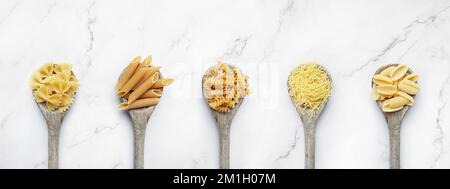 Verschiedene Arten von ungekochten Vollkornpasta in Holzlöffeln auf grauem Hintergrund Stockfoto