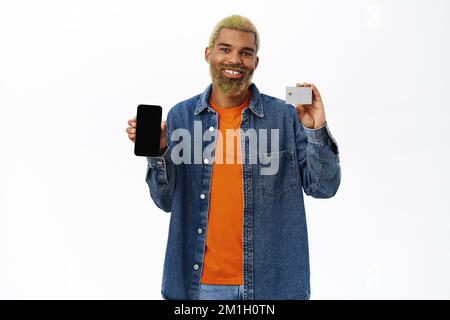 Ein schwarzer, eleganter Kerl zeigt Handy und Kreditkarte mit verschiedenen Emotionen Stockfoto
