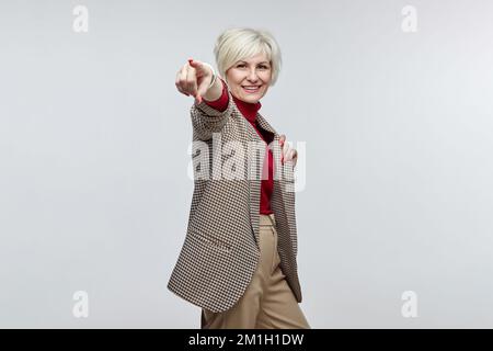 Eine schöne ältere Frau mit einem Lächeln zeigt mit dem Finger auf die Kamera. Das Konzept einer Geschäftsfrauenführerin. Stockfoto