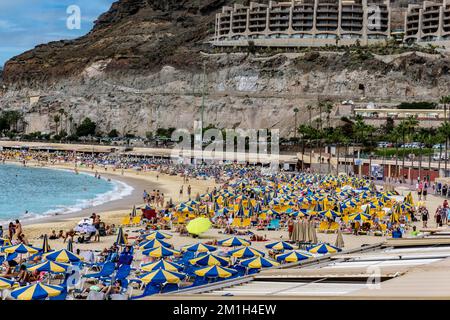 Der lebendige Strand und die atemberaubende Landschaft von Playa de Amadores auf Gran Canaria werden mit einem Farbtupfer zum Leben erweckt. Stockfoto