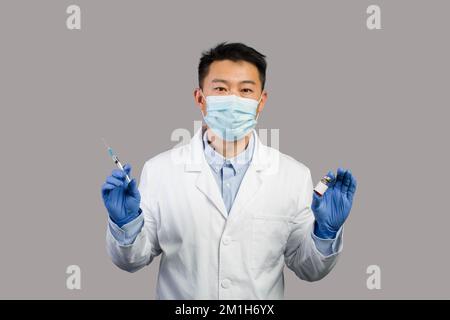 Seriöser reifer chinesischer Mann Therapeut in weißem Mantel, Schutzmaske zeigt Impfstoff und Spritze Stockfoto