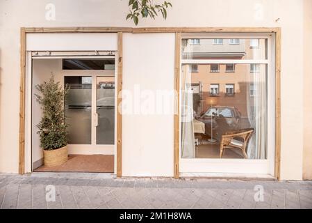 Fassade eines Geschäftsgeländes mit Blick von der Straße mit einer weißen Wand, Bambusrahmen und einem kleinen Olivenbaum Stockfoto