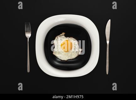 Spiegeleier auf einem schwarz-weißen Teller, serviert an einem schwarzen Tisch Stockfoto