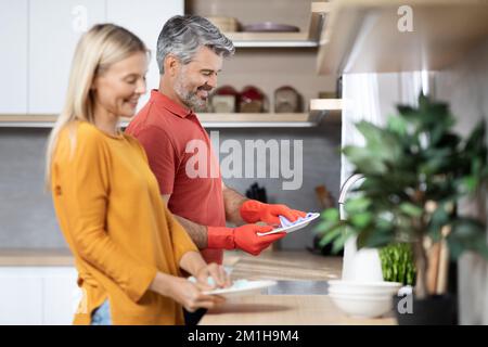 Glückliche, reife Ehepartner, die zusammen arbeiten, Geschirr spülen Stockfoto