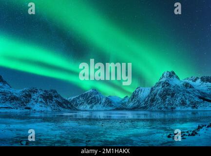 Aurora borealis über verschneite Berge, gefrorene Meeresküste Stockfoto