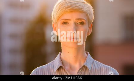 Außenportrait kaukasische Geschäftsfrau Erwachsene Geschäftsfrau Chef Lehrer im Freien stehend Sonnenuntergang Sonnenstrahlen Sonnenlicht Blick auf die Kamera. Nahaufnahme Stockfoto