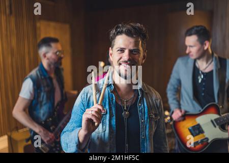 Musikband mit Wiederholungen, Schlagzeuger, der vorne steht und Stöcke hält, Gitarristen und ein Solist im Hintergrund. Hochwertiges Foto Stockfoto