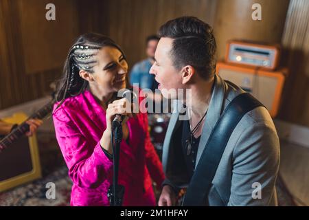 Innenporträt von ein paar Musikern, die während eines Konzerts Spaß haben. Junge, stilvolle weibliche Sängerin, die den männlichen Gitarrist ermutigt, mit ihr zu singen. Hochwertiges Foto Stockfoto