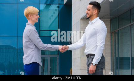 Zwei multiethnische Kollegen arabischen Mann und kaukasische Frau Geschäftspartner stehen im Freien in der Nähe von Firmengebäude reden schütteln Hände schließen Deal Stockfoto