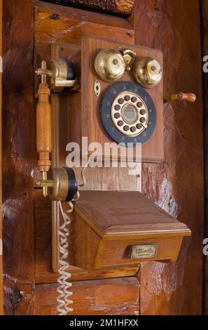 Antikes, an der Wand montiertes Telefon im Flur im alten Kanadiana-Blockhaus aus den 1800er Jahren. Stockfoto