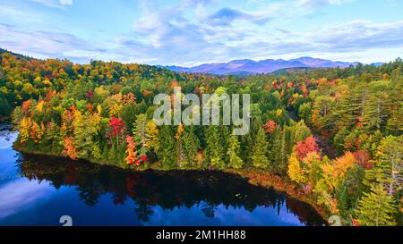 Luftfahrt über den blauen See mit herbstlichen Waldhügeln und Bergen in der Ferne Stockfoto