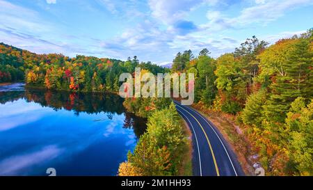 Luftfahrt über der Straße neben dem blauen See und umgeben von Herbstwäldern Stockfoto