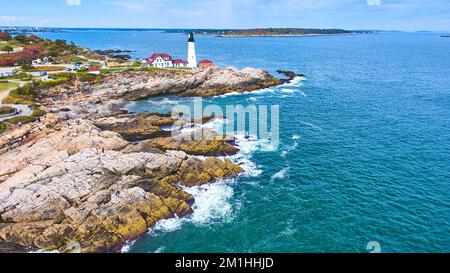 Atemberaubender Blick aus der Vogelperspektive auf die felsige Küste von Maine mit stürmischen Wellen und weißem Leuchtturm Stockfoto