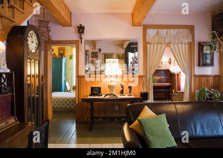 Großvateruhr und dunkelbraunes Ledersofa im Wohnzimmer in einem alten Haus im viktorianischen Landhausstil aus dem Jahr 1904. Stockfoto