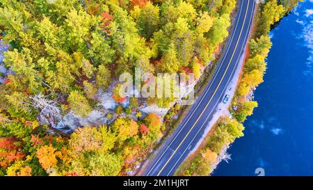 Luftblick auf die Straße neben dem See und umgeben von Herbstlaub und Felsen Stockfoto