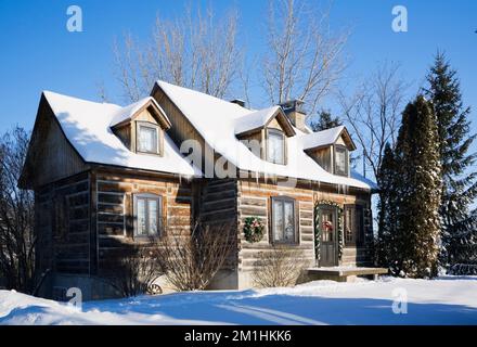 1982 erbaute Nachbildung des 1800er Canadiana zweistöckigen Blockhauses mit Weihnachtsdekorationen im Winter. Stockfoto