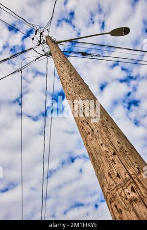 Details, die nach einem strukturierten Telefonmast aus Holz mit fleckigen Wolken am blauen Himmel suchen Stockfoto