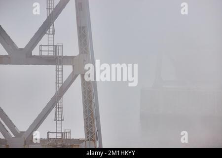 Stützpfeiler der alten Stahlbrücke mit Leitern, die bei extremen Wetterbedingungen verblassen, nebeliger Morgen Stockfoto