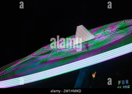 Rotierende Karnevalslichter verschwommen in der Nacht von Grün und Violett Stockfoto