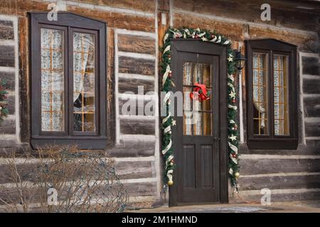 Eingangstür auf 1982 erbaute Nachbildung von 1800er Canadiana zweistöckiges Blockhaus mit Weihnachtsdekorationen im Winter. Stockfoto