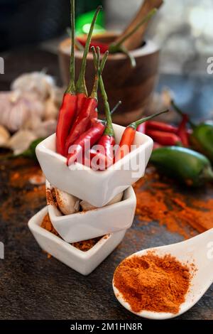 Rote, heiße Chili-Paprika in einer Schüssel mit Holzmörtel und Pistille im Hintergrund mit Knoblauch Stockfoto