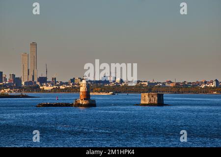 Robbins Reef Lighthouse in New York City mit goldenem Licht und Industriestadt dahinter Stockfoto