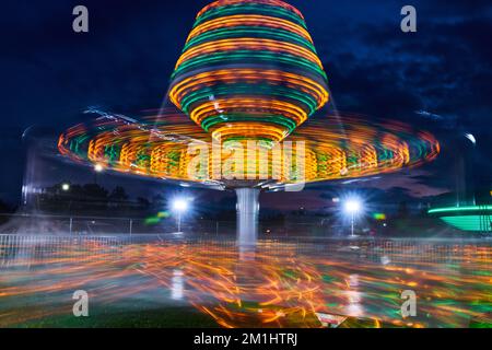 Verschwommene gelbe und grüne Lichter des Karnevalsritts bei Nacht während der County Fair Stockfoto