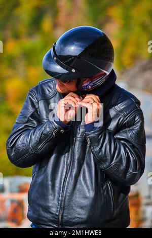 Vertikales Porträt eines unbekannten Motorradfahrers, der einen schwarzen Helm mit American Flag und eine schwarze Lederjacke aufsetzt Stockfoto