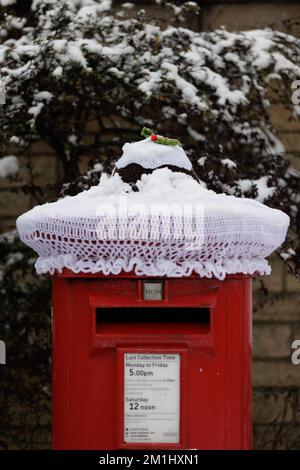 Festliche Weihnachtsdekorationen auf der Straße auf einem Briefkasten an einem Wintertag mit Schnee. Gestrickter/gehäkelter Weihnachtspudding. Stockfoto