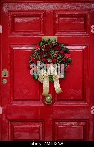 Kranz an einer roten Tür. Traditionell, altmodisch. Festliche Weihnachtsdekorationen auf der Straße an einem Wintertag mit Schnee Stockfoto