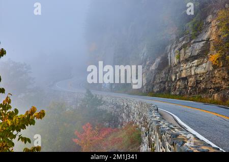 Steinmauer entlang der atemberaubenden Straße gegen die Klippen, die sich in Nebel verschlängeln Stockfoto