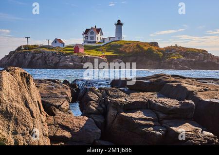 Der Leuchtturm von Maine liegt auf einer Insel von der felsigen Küste des Festlands mit Wellen, die Spalten füllen Stockfoto