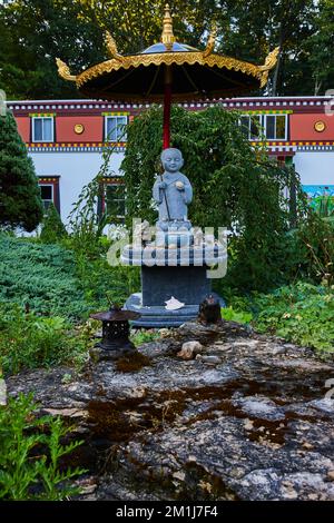 Religiöse Statue im Garten mit goldenem Regenschirm Stockfoto