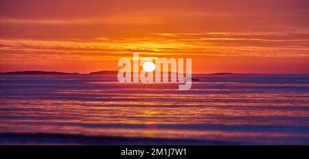 Goldenes Licht über dem Ozean an der Ostküste mit Sonnenaufgang und Details der Sonne und des Fischerschiffs in der Ferne Stockfoto