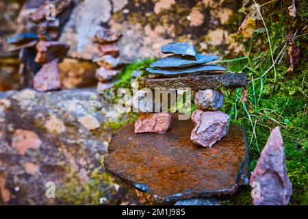 Kleine Steinsteine gestapelte Cairn in wunderschöner Form gegen Flechten bedeckte Steine und Moos Stockfoto