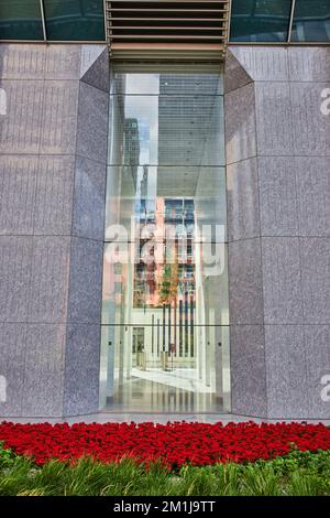 Blick nach außen großes Gebäude mit Glasblick in die schicke Lobby und rote Blumen draußen Stockfoto