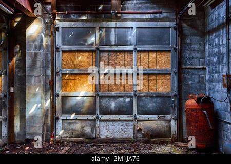Detail einer verlassenen Innenwerkstatt mit grauem Garagentor und roten Kanistern Stockfoto