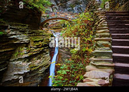 Steintreppen entlang der Schlucht mit Steinbogen-Wanderbrücke und Wasserfällen durch die Schlucht im Bundesstaat New York Stockfoto