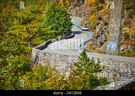 Straße mit Steinmauer, die sich durch Klippen im Wald schlängelt Stockfoto