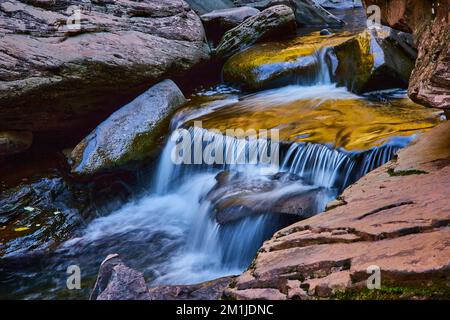 Sanftes, warmes Licht über einem wunderschönen kleinen, kaskadierenden Wasserfall, umgeben von sanften Felsen Stockfoto