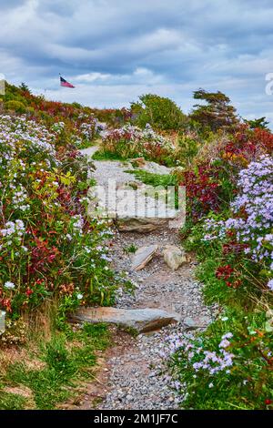 Schmaler Kiesweg in Maine, umgeben von Blumen und mit amerikanischer Flagge in der Ferne Stockfoto